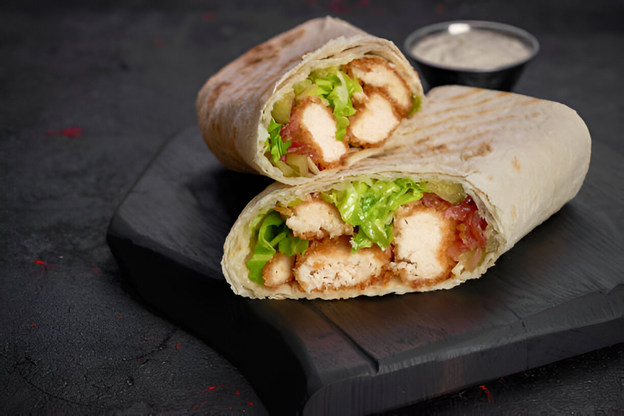 Two halves of a bread wrap filled with lettuce, crispy chicken, and other ingredients on a black serving board.
