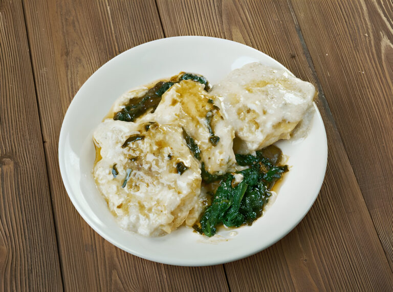 A plate of fluffy dumplings covered in a green sauce with leafy greens on the side.