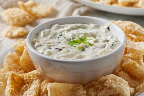 A bowl of creamy dip surrounded by crispy snacks.