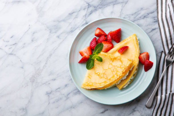 A plate of two golden crepes garnished with fresh strawberries and a sprig of mint.