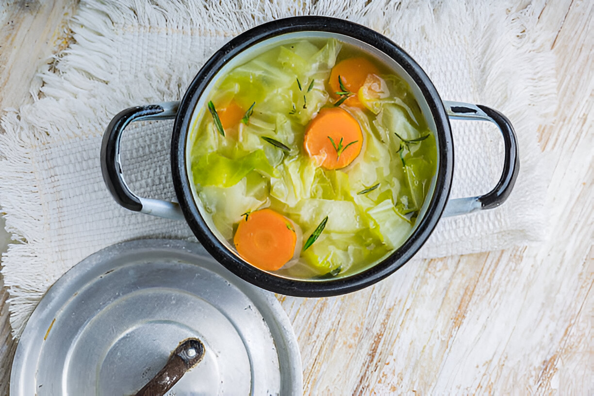 A pot of delicious vegetable soup with carrots and cabbage on a textured white cloth.