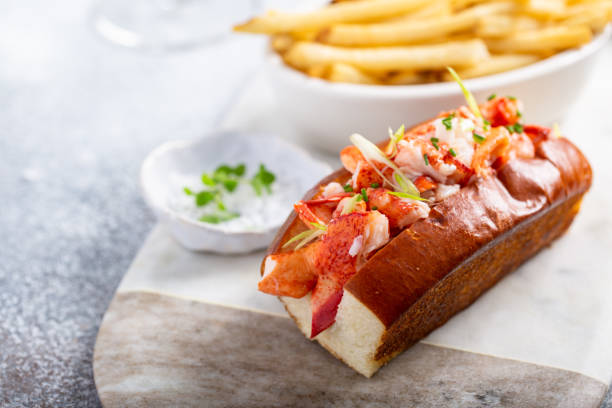 A gourmet lobster roll topped with fresh lobster meat, served with a side of fries and a small bowl of herbs.