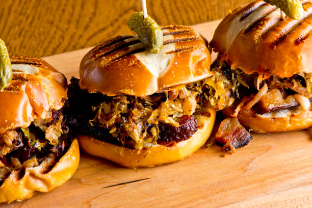 Three gourmet sliders on a wooden board, topped with pickles.