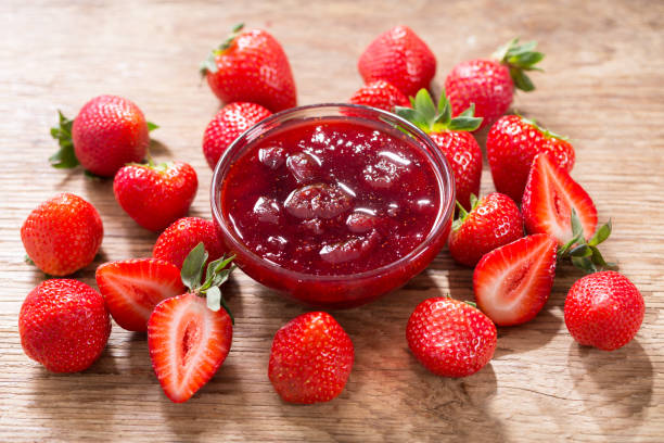 A bowl of strawberry jam surrounded by fresh strawberries on a wooden surface