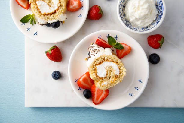 A delicious dessert featuring a slice of cake roll topped with whipped cream and accompanied by fresh strawberries and blueberries.