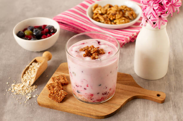 A glass of yogurt topped with granola, surrounded by bowls of fruit and a flower vase.