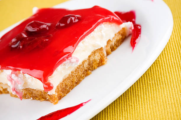 A slice of cheesecake topped with bright red cherry gelatin on a white plate