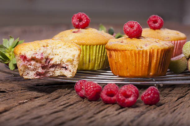 A plate of freshly baked raspberry muffins with one cut in half, showcasing the raspberry filling, placed on a rustic wooden table.