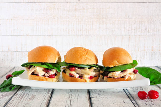 Three chicken salad sandwiches with spinach and cranberries on a white tray