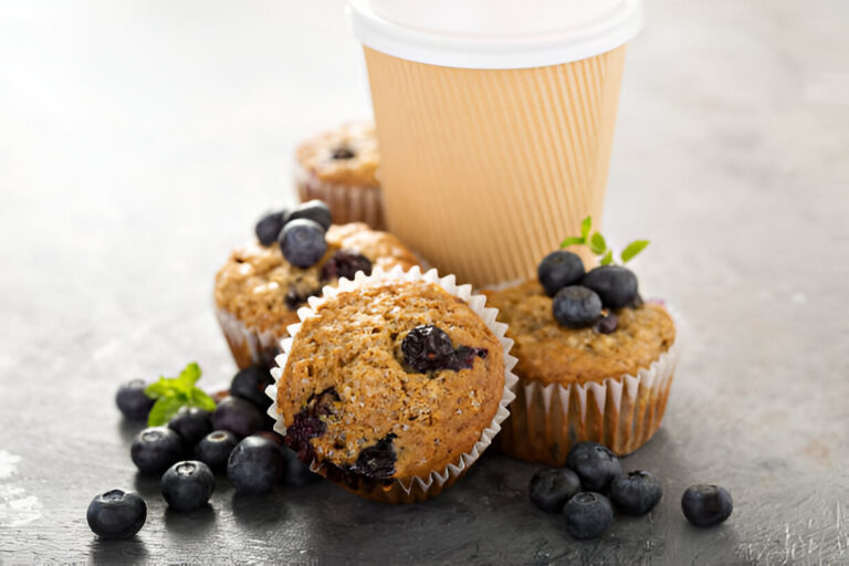 A collection of blueberry muffins with a coffee cup and fresh blueberries on a textured surface.