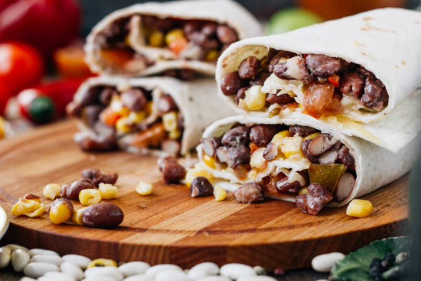 Delicious burritos filled with black beans, corn, and cheese on a wooden cutting board.