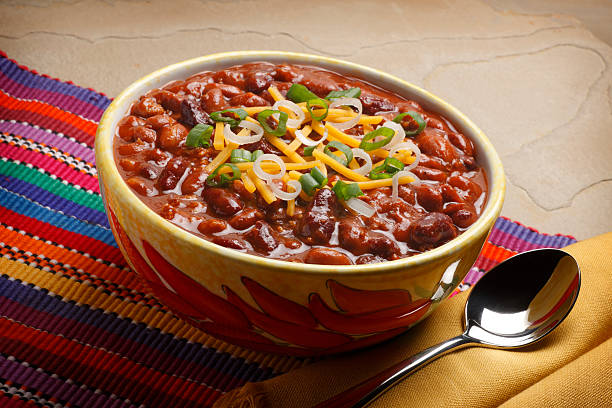 A colorful bowl of chili topped with shredded cheese and green onions, placed on a vibrant woven tablecloth.