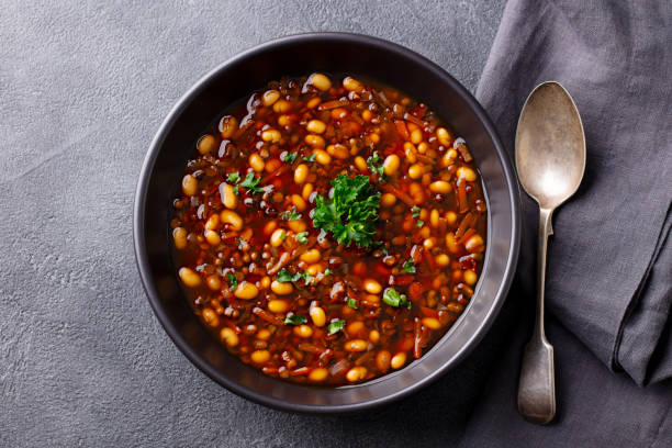 A bowl of soup with beans and herbs on a gray background