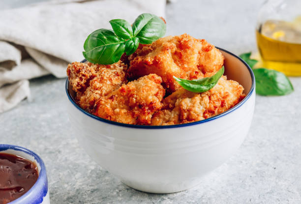 A bowl of crispy fried chicken garnished with fresh basil leaves, placed on a light-toned surface.