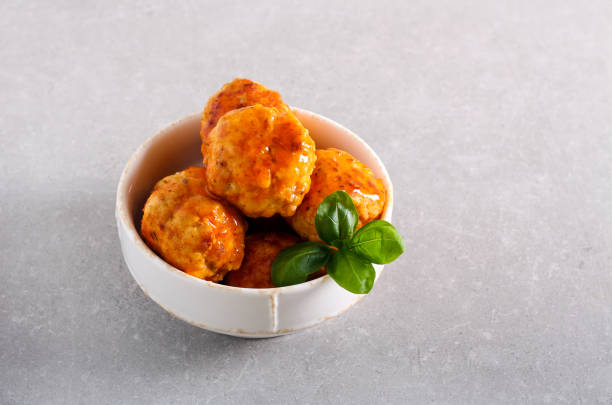 A bowl filled with delicious meatballs coated in a savory sauce, garnished with fresh basil leaves.