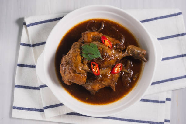 A bowl of chicken stew topped with sliced red chilies and parsley on a striped napkin