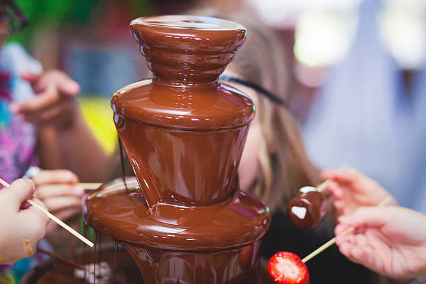 Chocolate fountain with various foods being dipped, including strawberries and bananas.