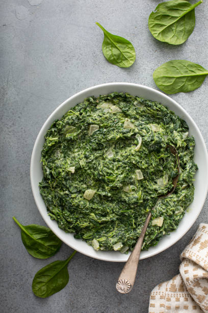 A bowl of creamy spinach dip with fresh spinach leaves scattered around