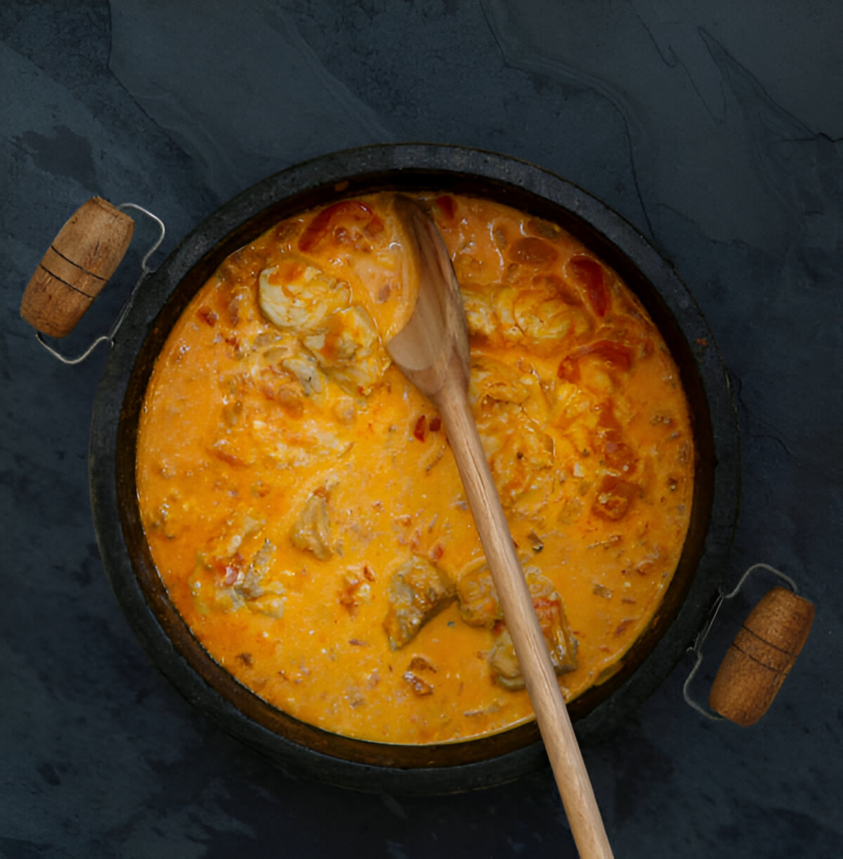 A simmering pot of creamy orange stew with a wooden spoon resting inside