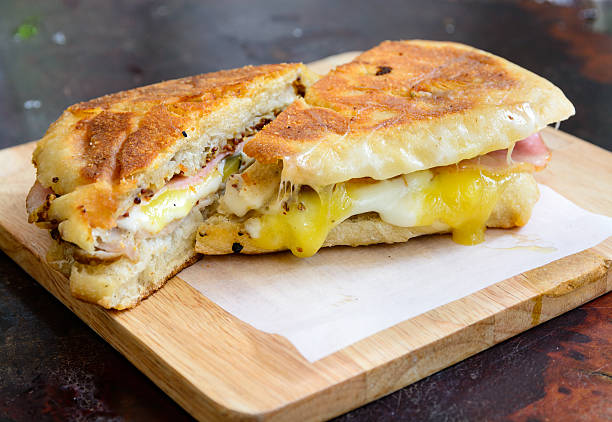 A delicious sandwich cut in half showcasing layers of ham, cheese, and egg on a wooden board.