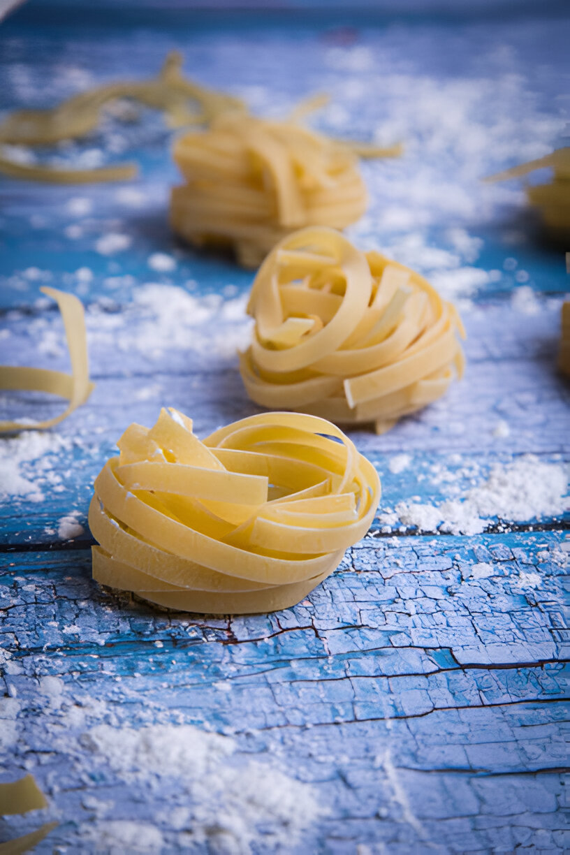 Raw fettuccine noodles arranged on a blue wooden surface sprinkled with flour