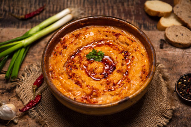 A bowl of smooth, spicy hummus topped with olive oil and a sprinkle of herbs, served with bread and vegetables.