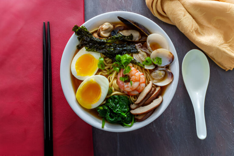 A delicious bowl of ramen featuring noodles, shrimp, soft-boiled eggs, and various toppings such as seaweed and vegetables.