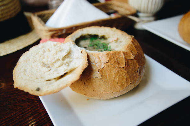 A bread bowl filled with a creamy soup, with a lid resting beside it on a white plate.