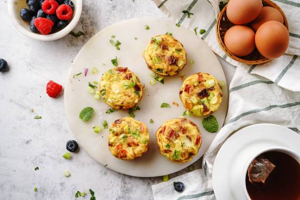 A top view of mini vegetable and bacon frittatas on a round serving plate, surrounded by fresh berries and a cup of tea.