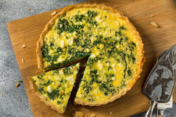 A freshly baked spinach quiche on a wooden cutting board with a slice removed.