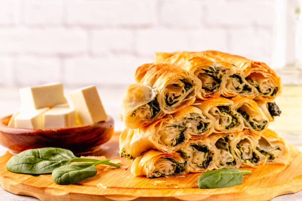 A neatly stacked plate of savory spinach pastries beside a bowl of cubed feta cheese.