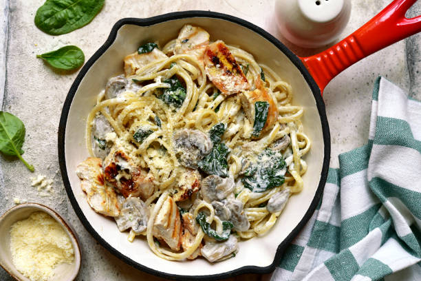 A delicious plate of creamy chicken and spinach pasta served in a red skillet with grated cheese on top.