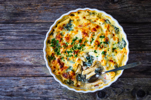 A creamy pasta bake topped with melted cheese and fresh parsley in a white ceramic dish on a wooden table