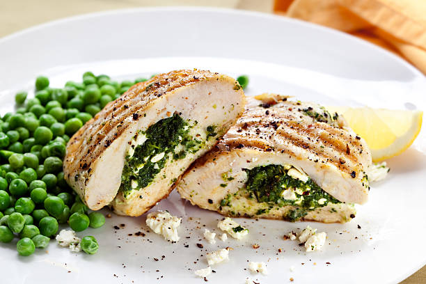 Grilled chicken breast stuffed with spinach and cheese, served with green peas and a lemon wedge.