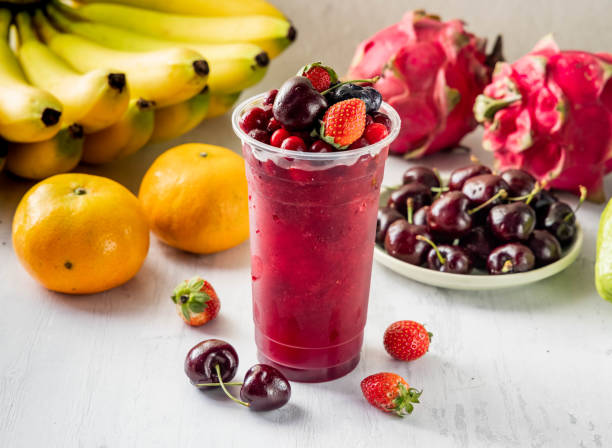 A colorful fruit drink in a clear cup surrounded by fresh fruits.