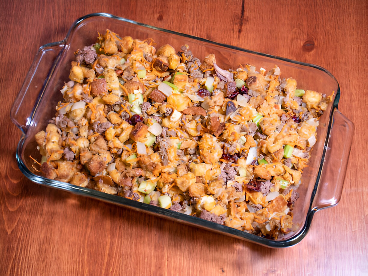 A glass baking dish filled with a mixture of stuffing, ground meat, celery, and spices.