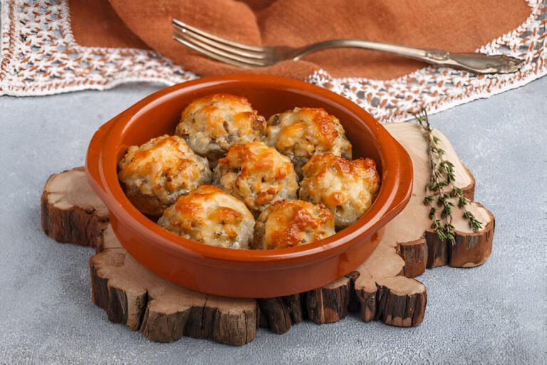 A warm dish of baked savory muffins in a brown ceramic serving bowl, placed on a wooden board with fresh herbs in the background.