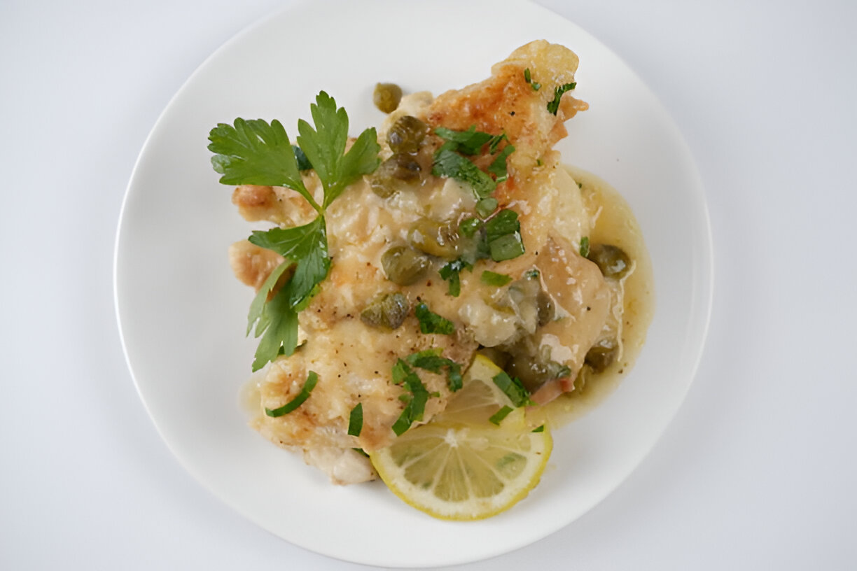 Delicious fish dish with capers and parsley on a white plate with a lemon slice