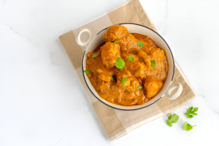Bowl of chicken curry with cilantro garnishing served on a neutral-toned background.