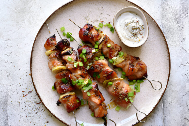 Grilled chicken skewers topped with green onions served with a yogurt sauce on a beige plate.