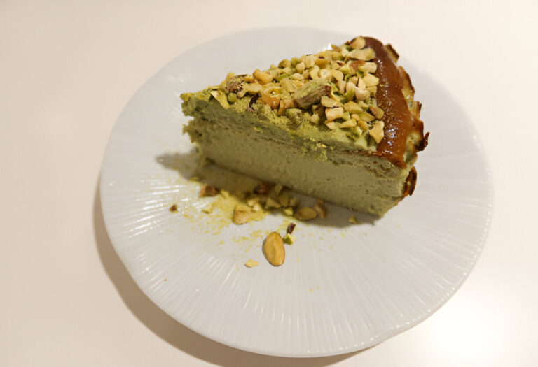 A slice of green cake topped with chopped nuts on a white plate.
