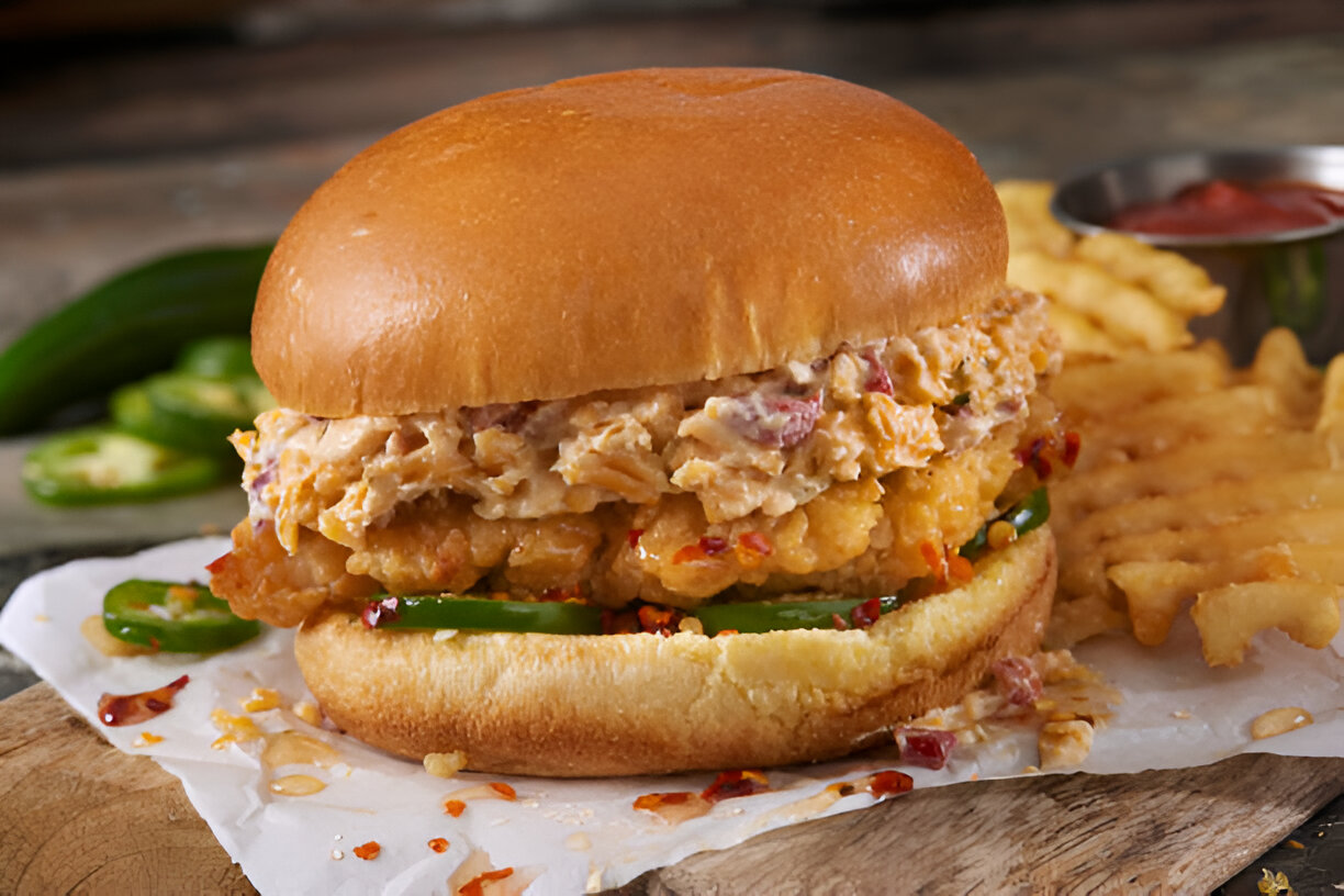 A close-up of a spicy chicken sandwich on a wooden surface, with crinkle-cut fries in the background.