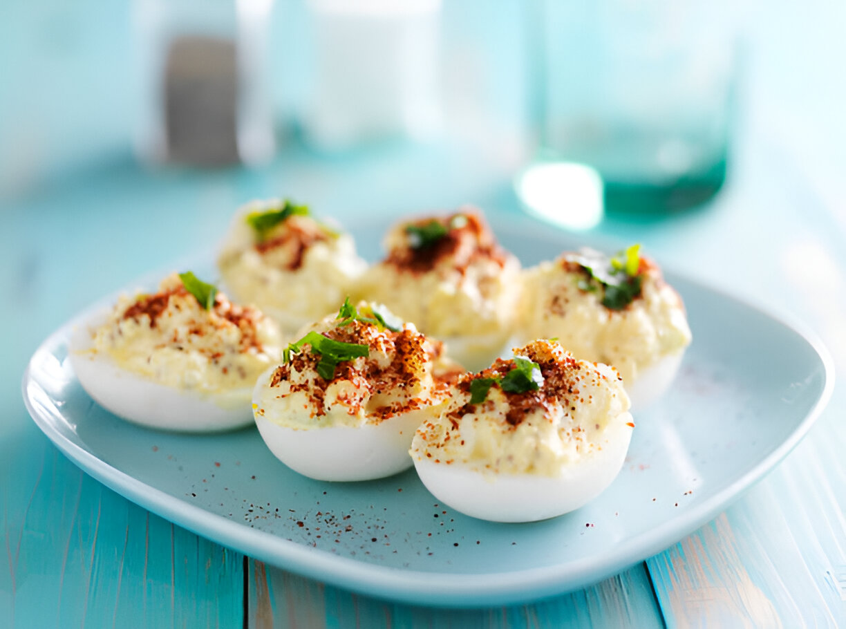 A plate of delicious deviled eggs garnished with spices and herbs, placed on a light blue surface.