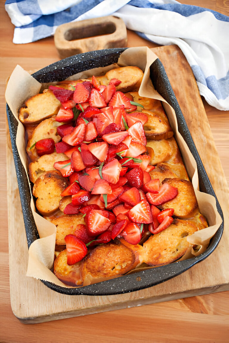 A freshly baked dish topped with sliced strawberries and mint leaves, served in a black baking dish.