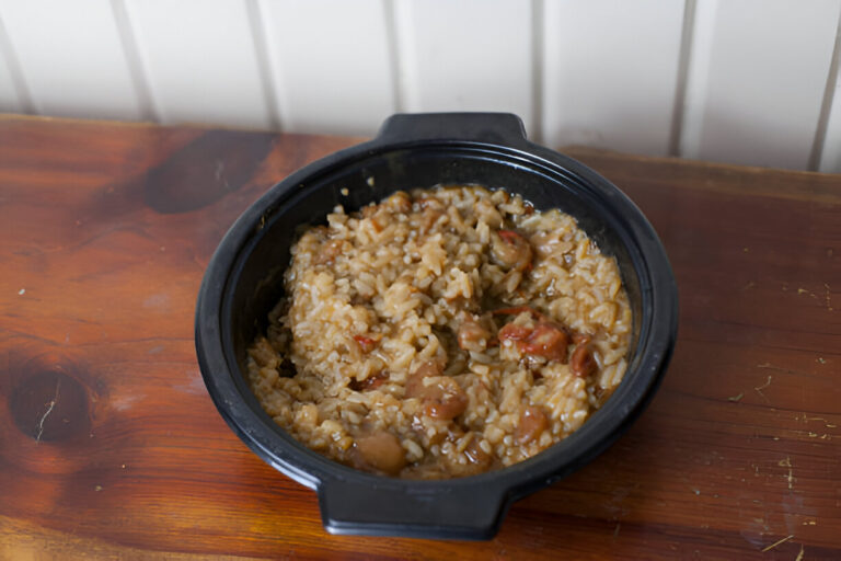 A black bowl filled with rice and meat dish, placed on a wooden table.