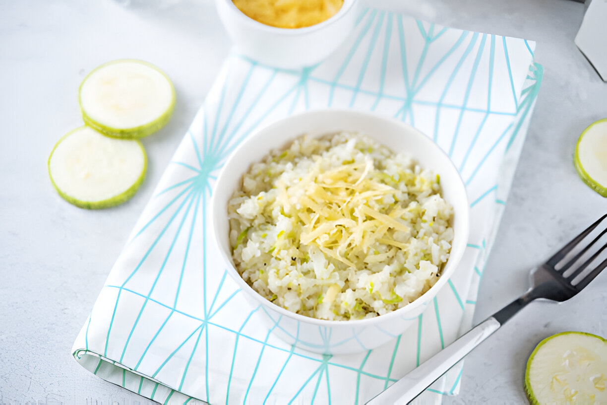 A bowl of rice mixed with chopped vegetables, garnished with shredded cheese, on a patterned napkin.
