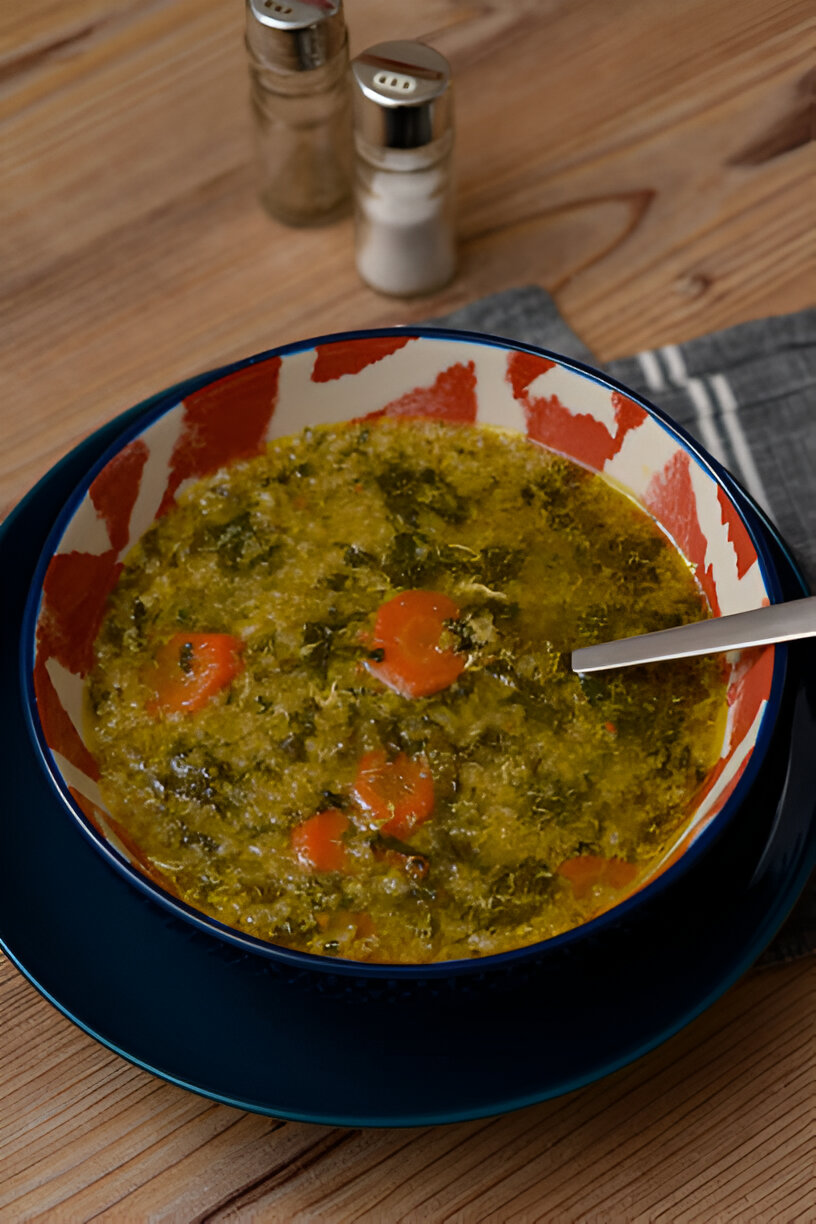 A bowl of green soup with carrots, served on a blue plate with salt and pepper shakers in the background.