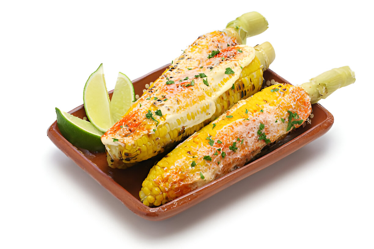 Two ears of elote topped with cheese and spices, served with lime wedges on a brown plate.