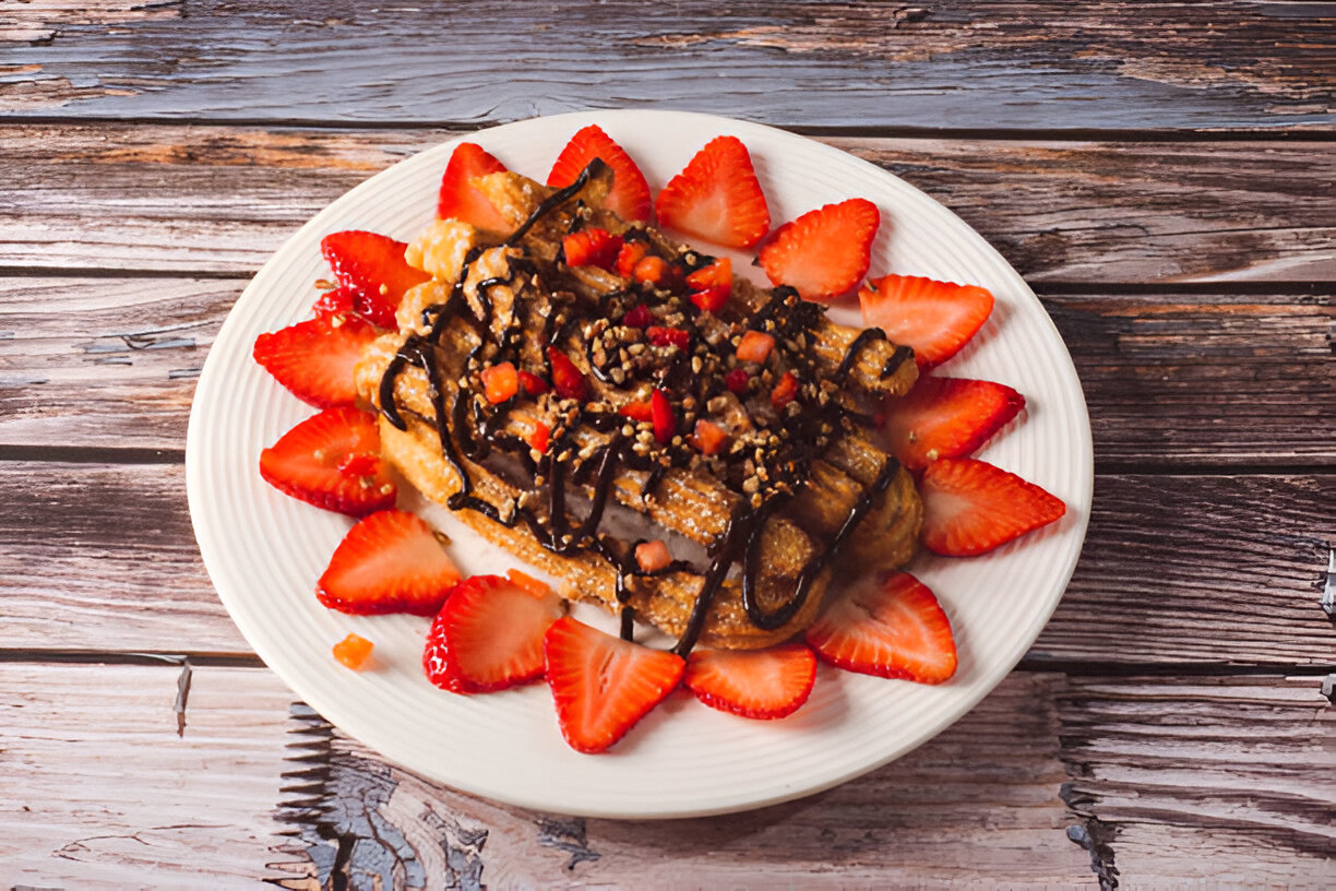 A delicious plate of churros topped with chocolate drizzle and fresh strawberries arranged around it.