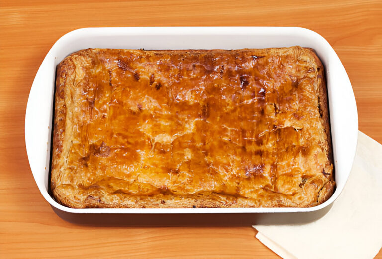 Golden-brown baked pastry in a white dish on a wooden surface.